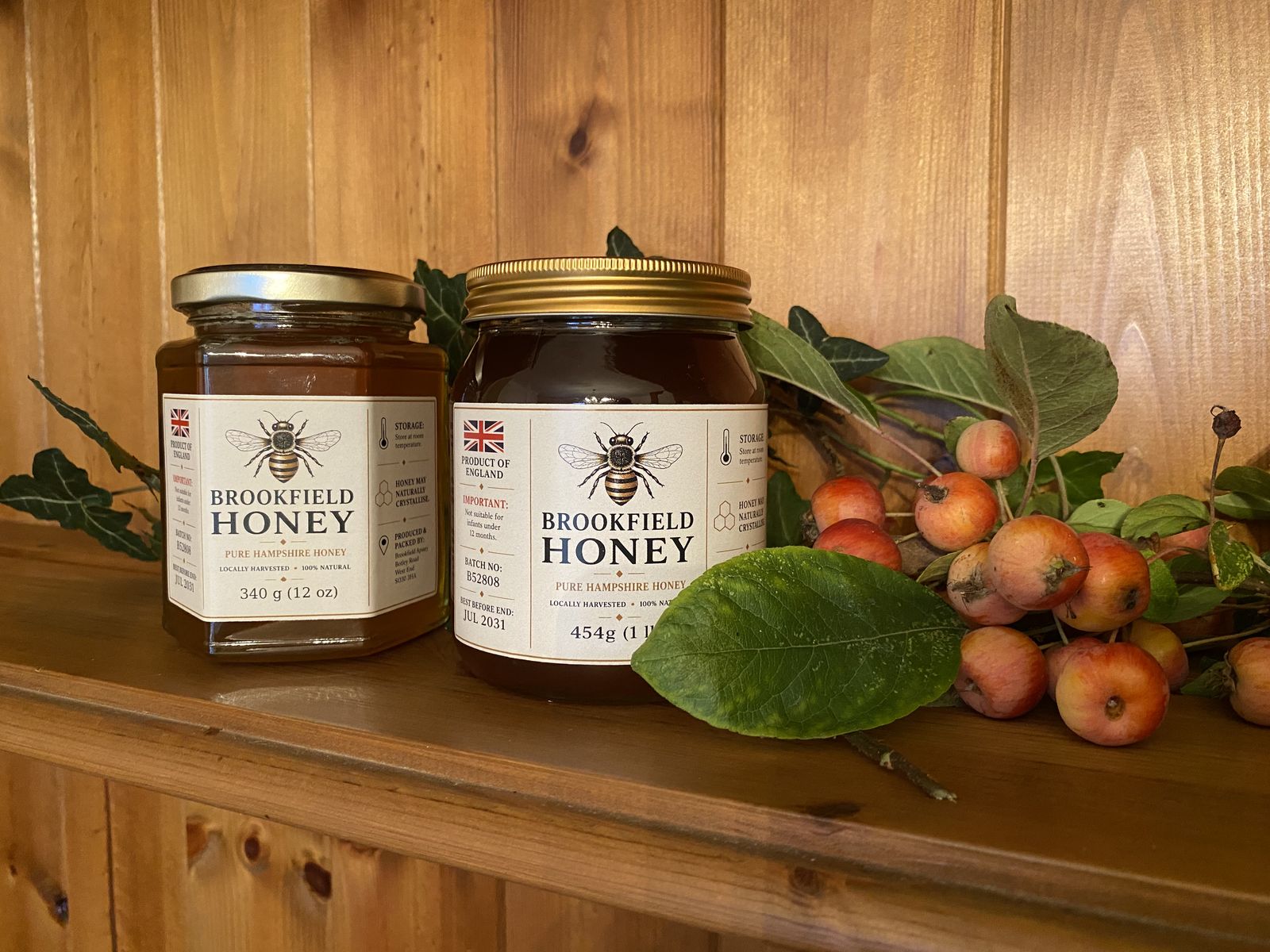 Two jars of Brookfield Honey on a wooden shelf with ivy leaves and crab apples